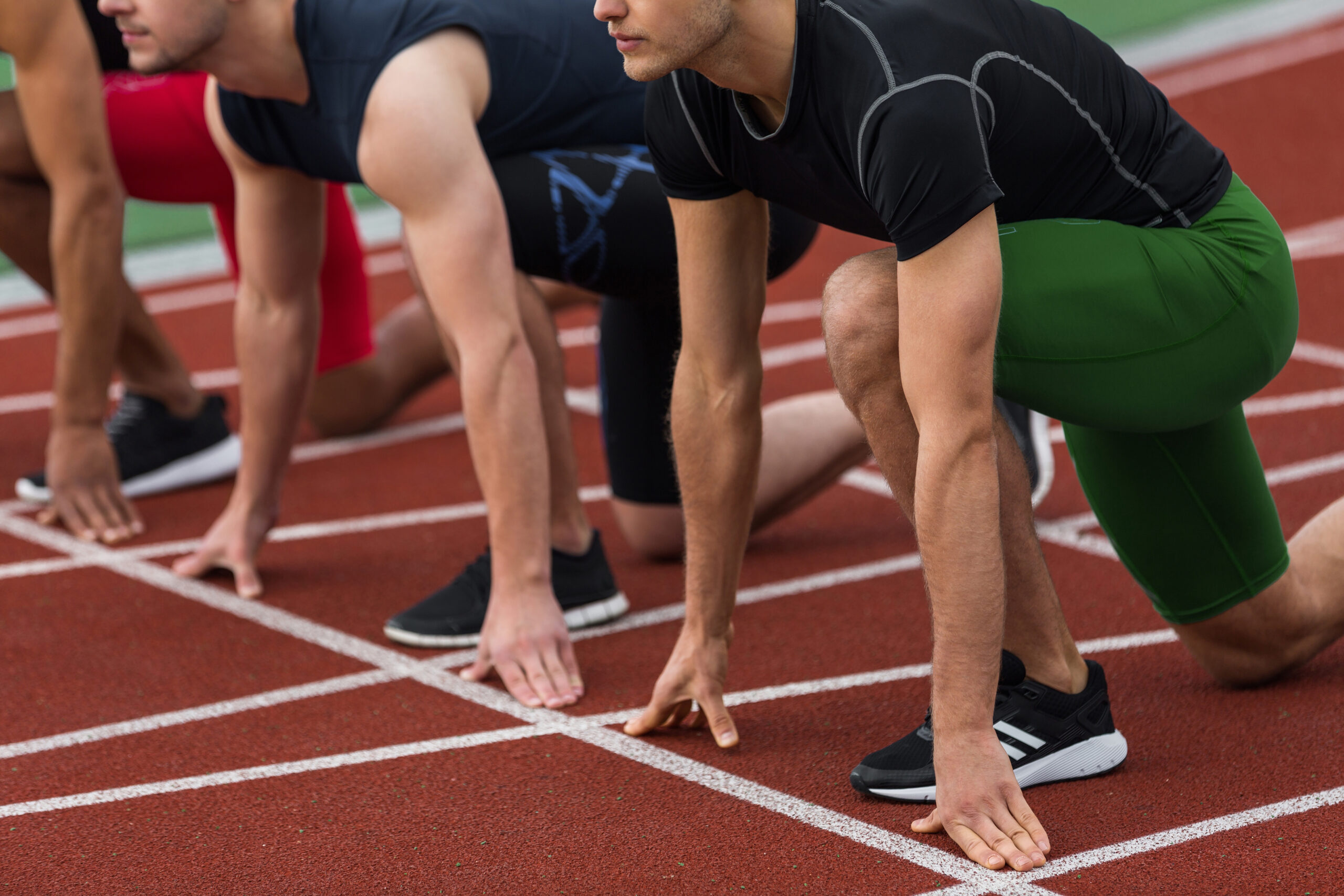 Cropped picture of multiethnic athlete group ready to run on running track outdoors.