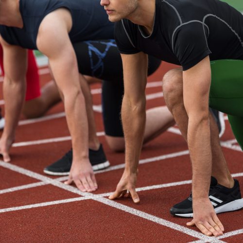 Cropped picture of multiethnic athlete group ready to run on running track outdoors.